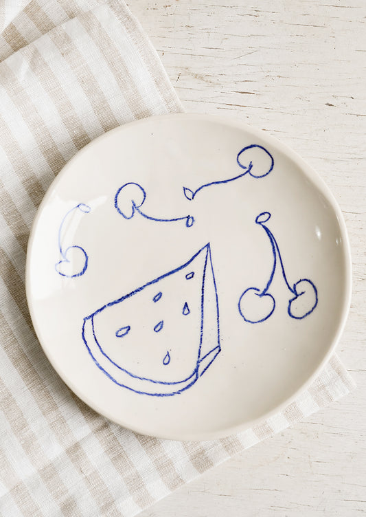 A ceramic side plate with still life fruit drawings in blue.