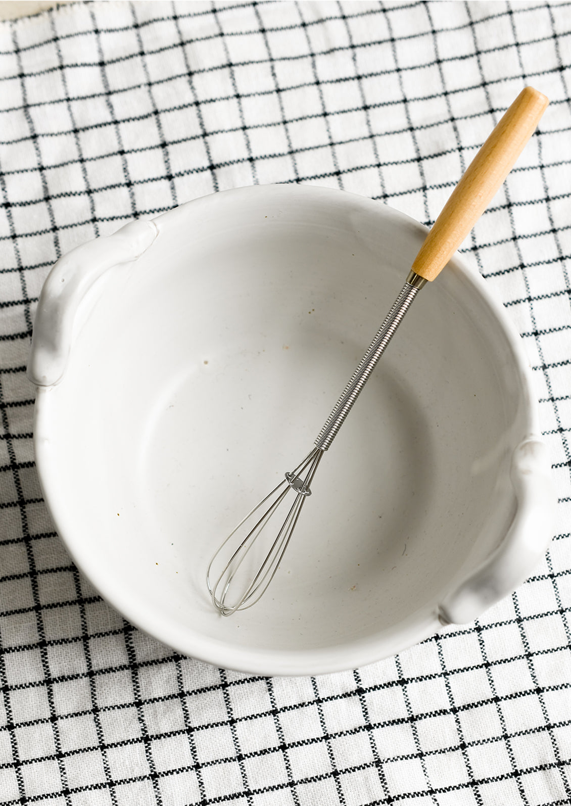 A white ceramic bowl with top handles that fit included whisk.