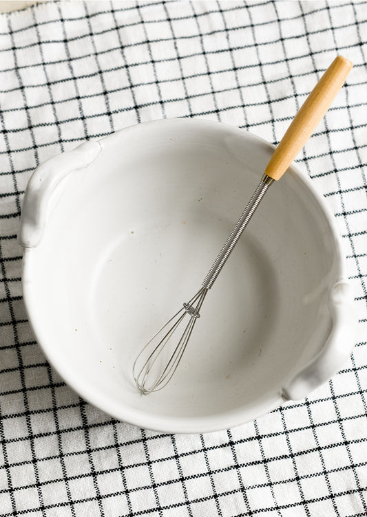 A white ceramic bowl with top handles that fit included whisk.