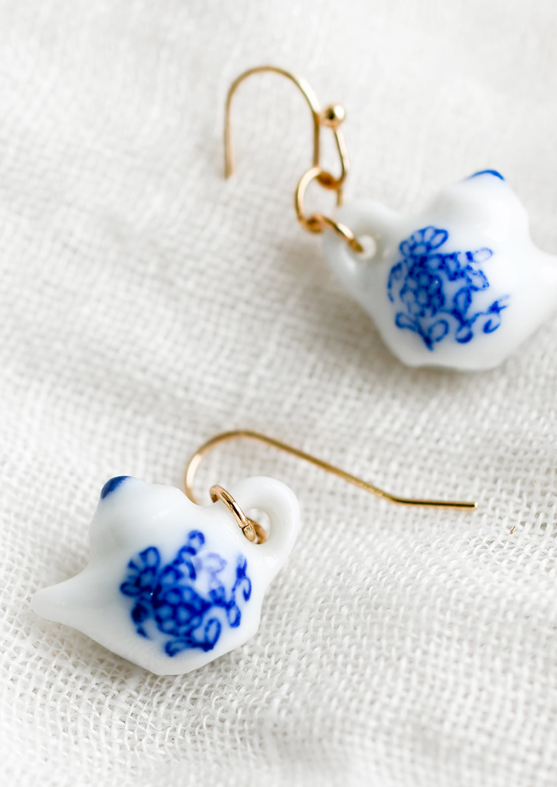 A pair of earrings in shape of white teapot with blue floral print.