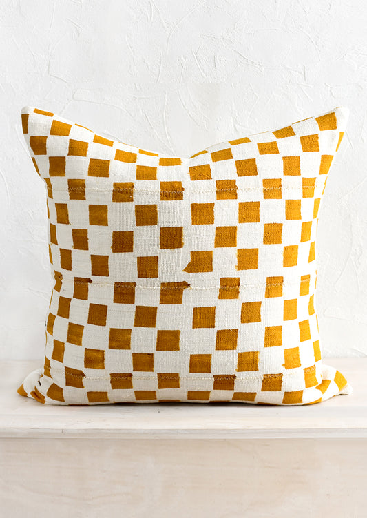 A square throw pillow in natural mudcloth with ochre checker print.