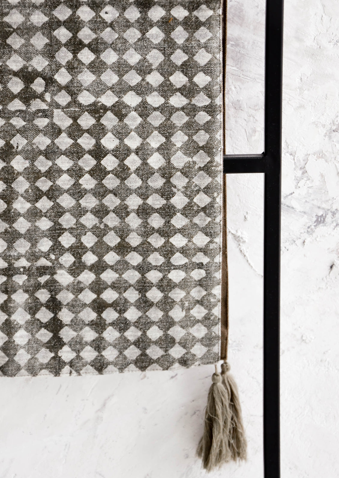 Table runner textile in distressed dark grey with white stamped diamond pattern, grey tassels at corners.