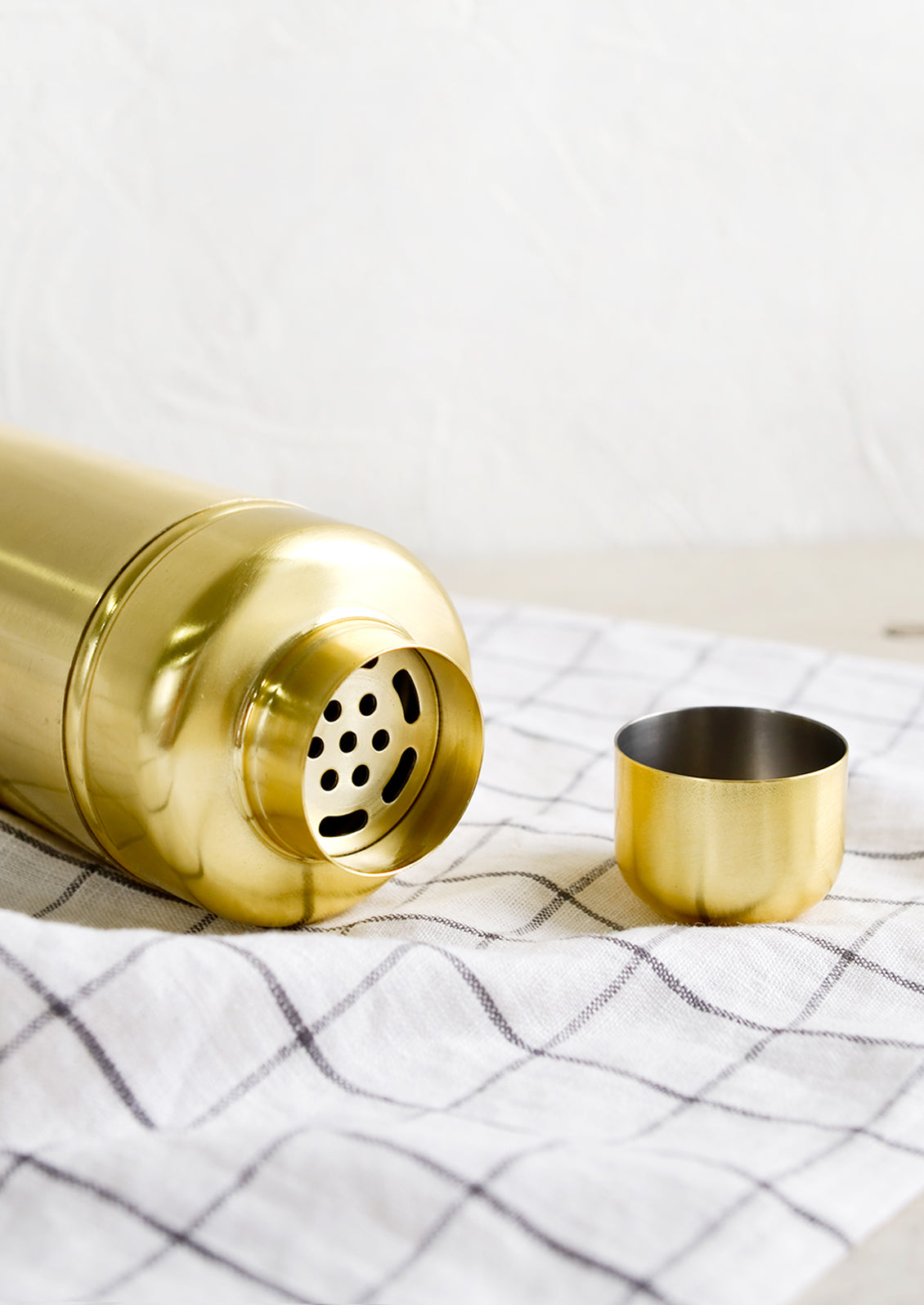 A cocktail shaker in satin gold metal with lid off.