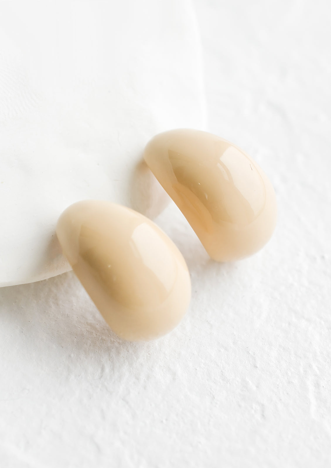 A pair of glossy ivory bean shaped earrings.