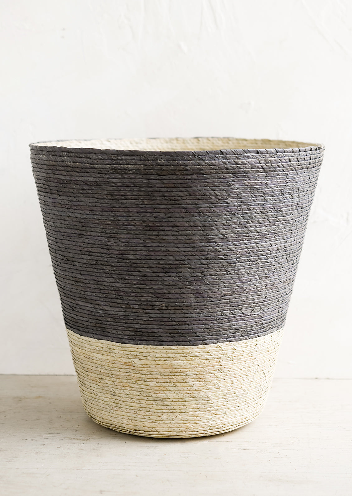 A conical shaped storage basket made from woven palm leaf in mineral blue & natural color way.