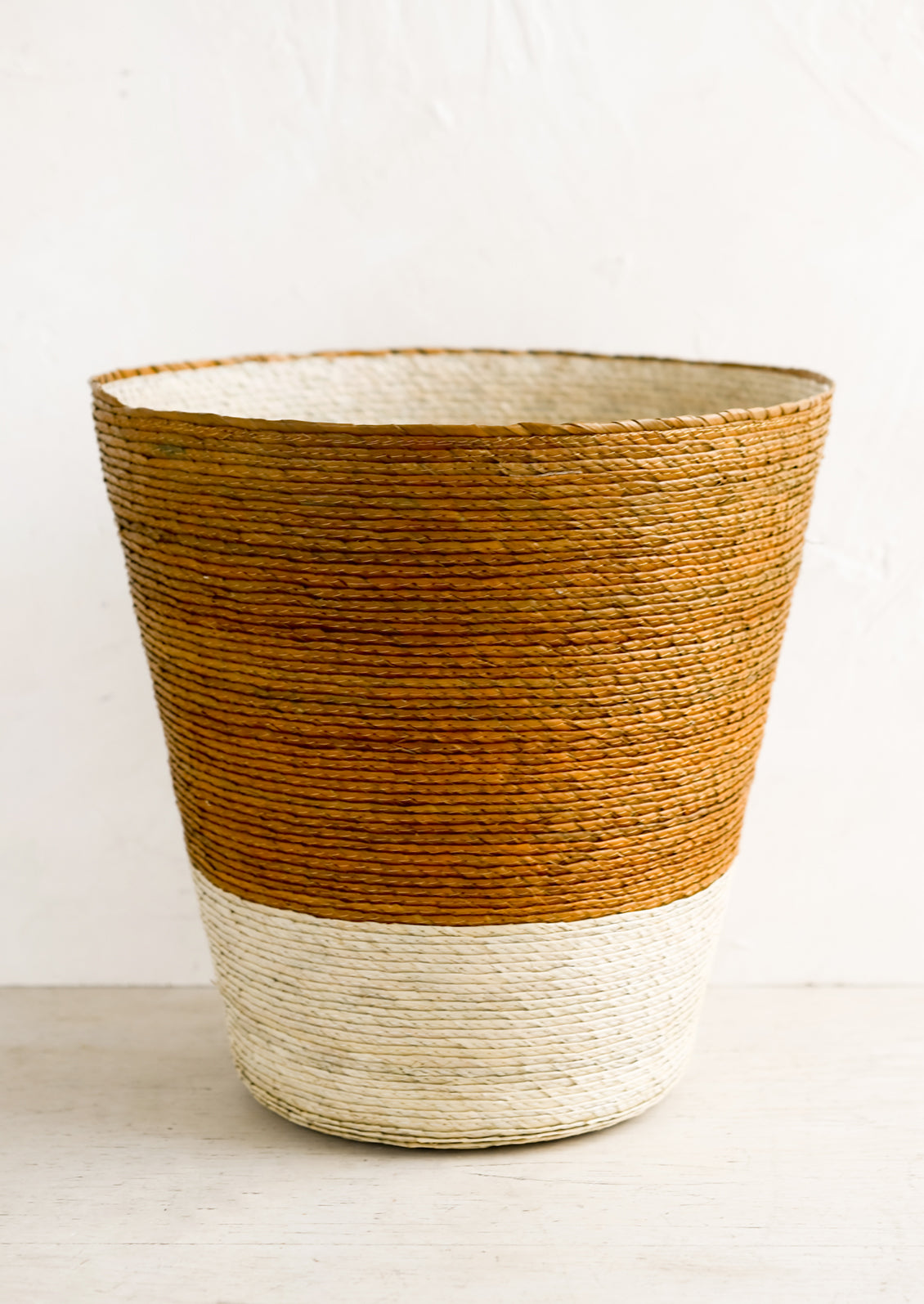 A conical shaped storage basket made from woven palm leaf in ochre & natural color way.