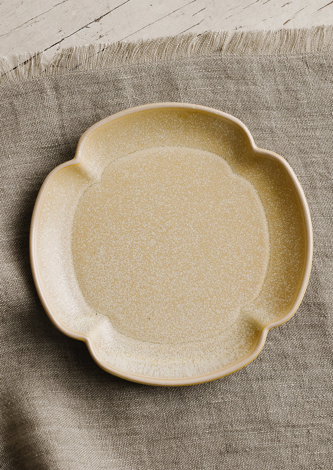 A quartrefoil shaped ceramic plate in sand color.