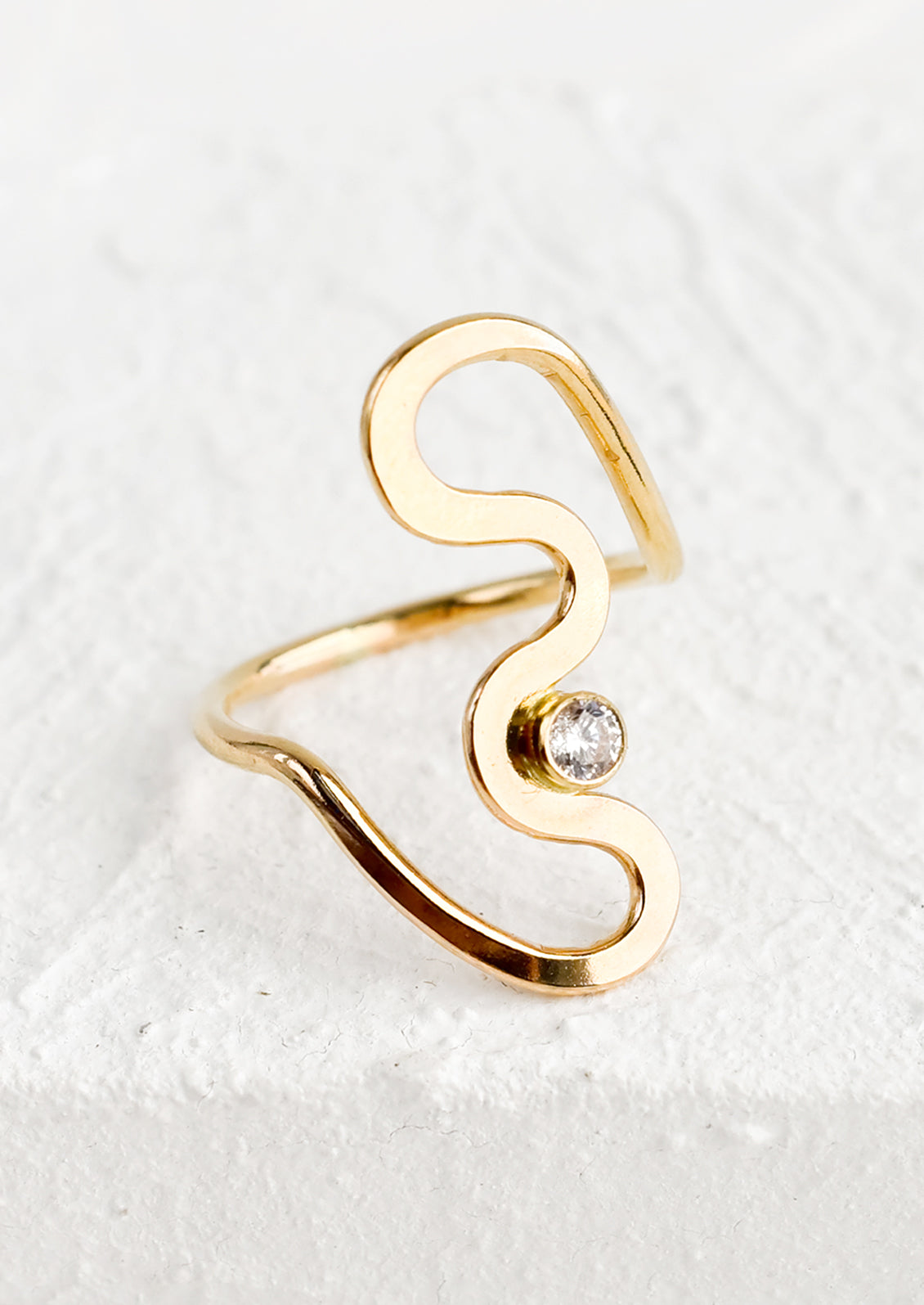 A gold ring in freeform squiggle shape with single bezel crystal at middle.