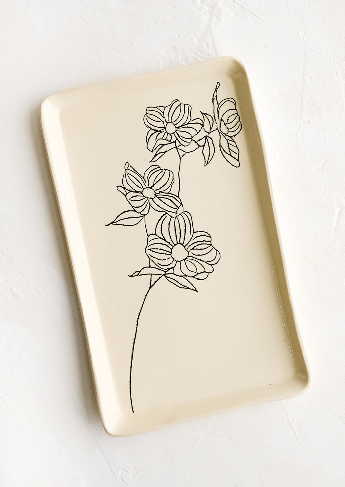 A rectangular ceramic tray in natural bisque color with an etched black drawing of dogwood flower.