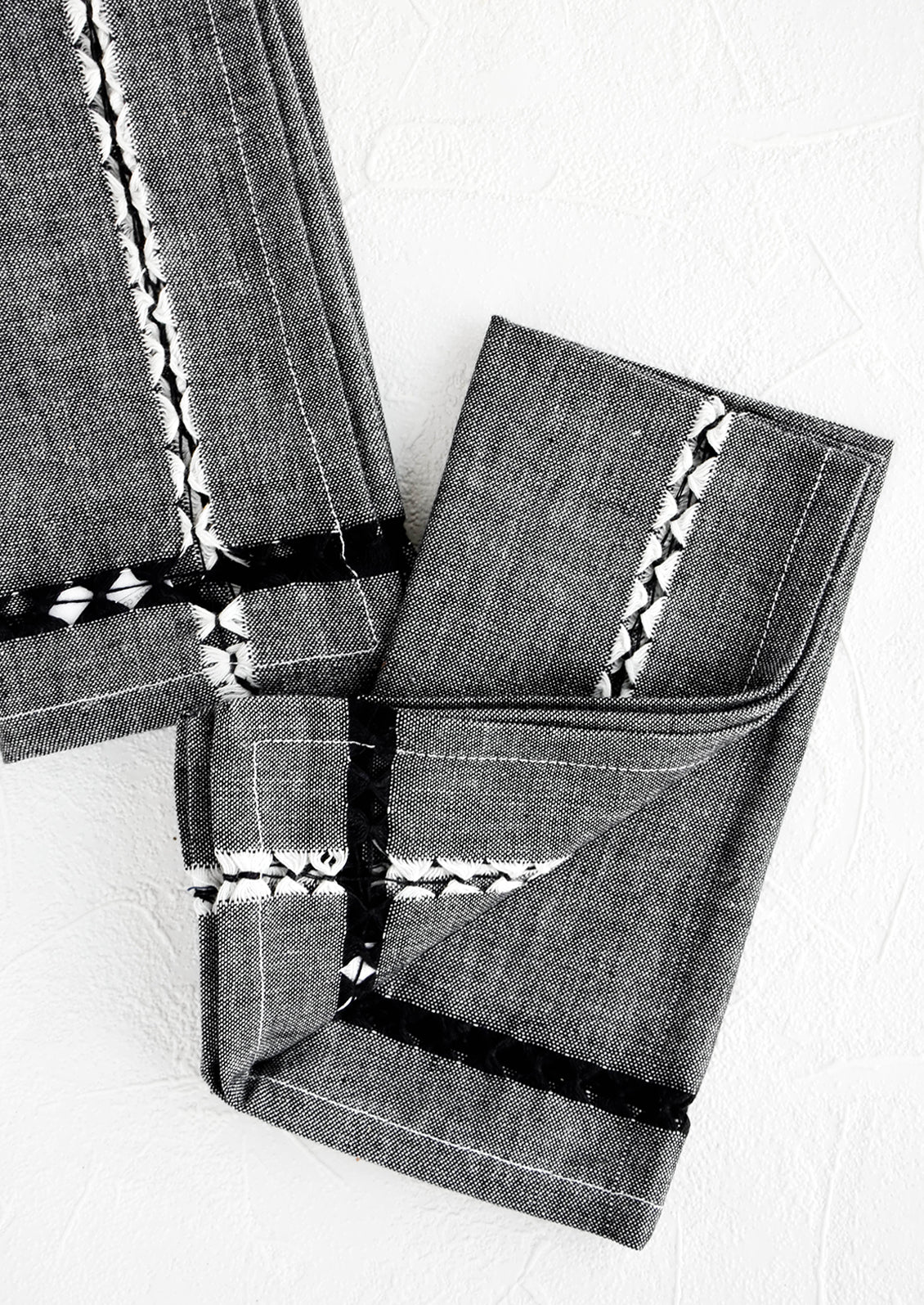 Pair of folded fabric dinner napkins in black chambray with geometric cutout detailing