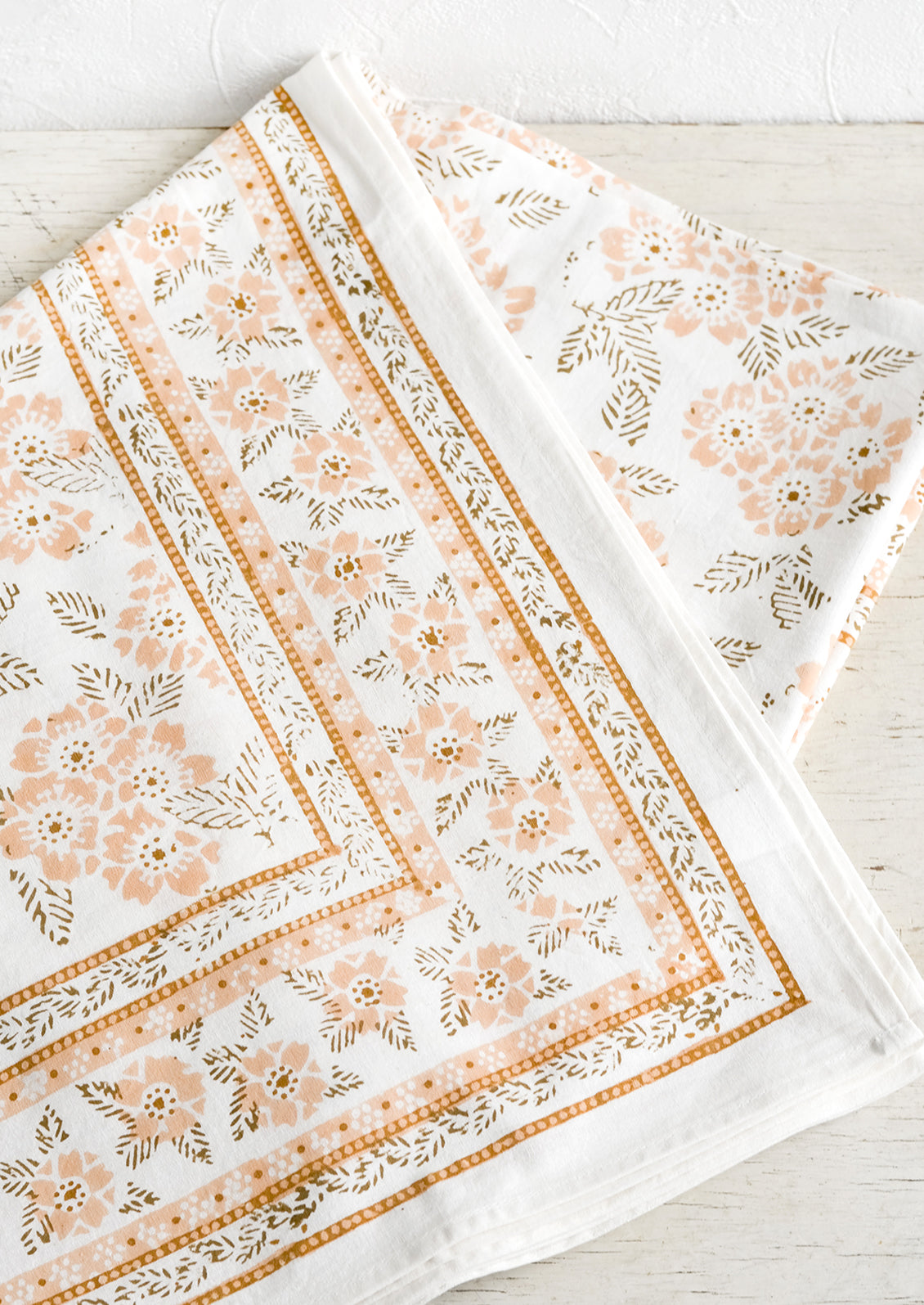 A block printed tablecloth with peach and brown floral print.