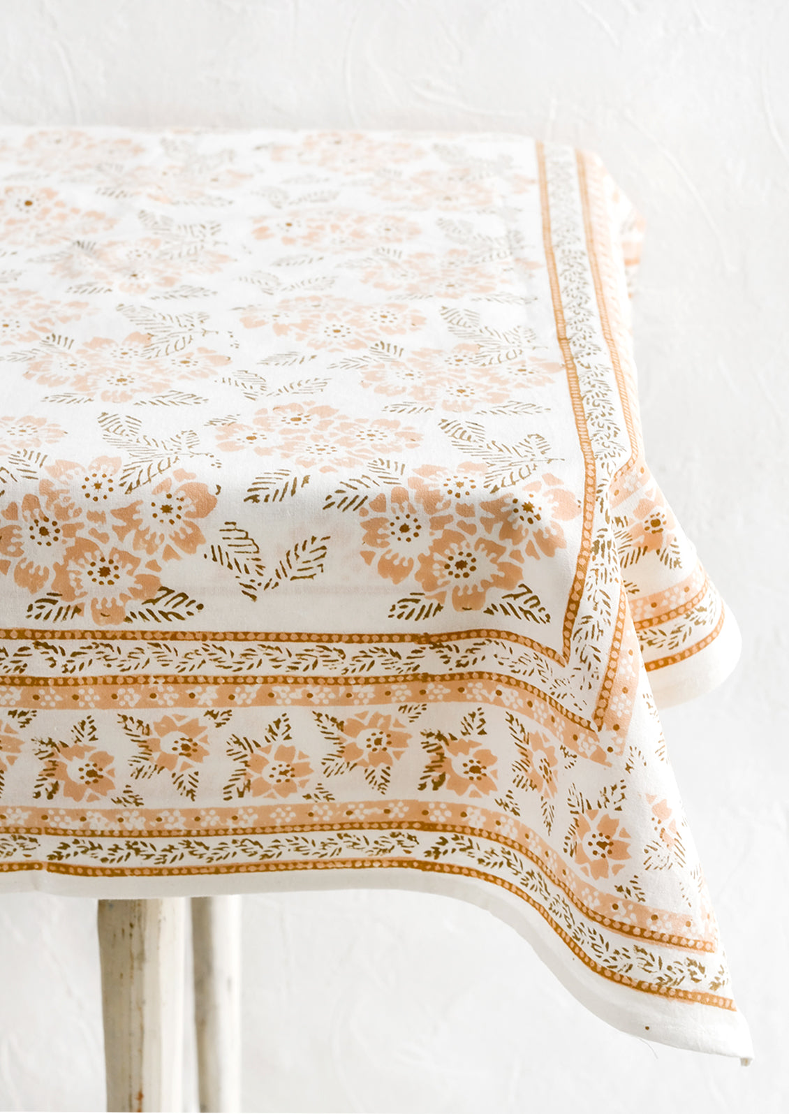 A block printed tablecloth with peach and brown floral print.