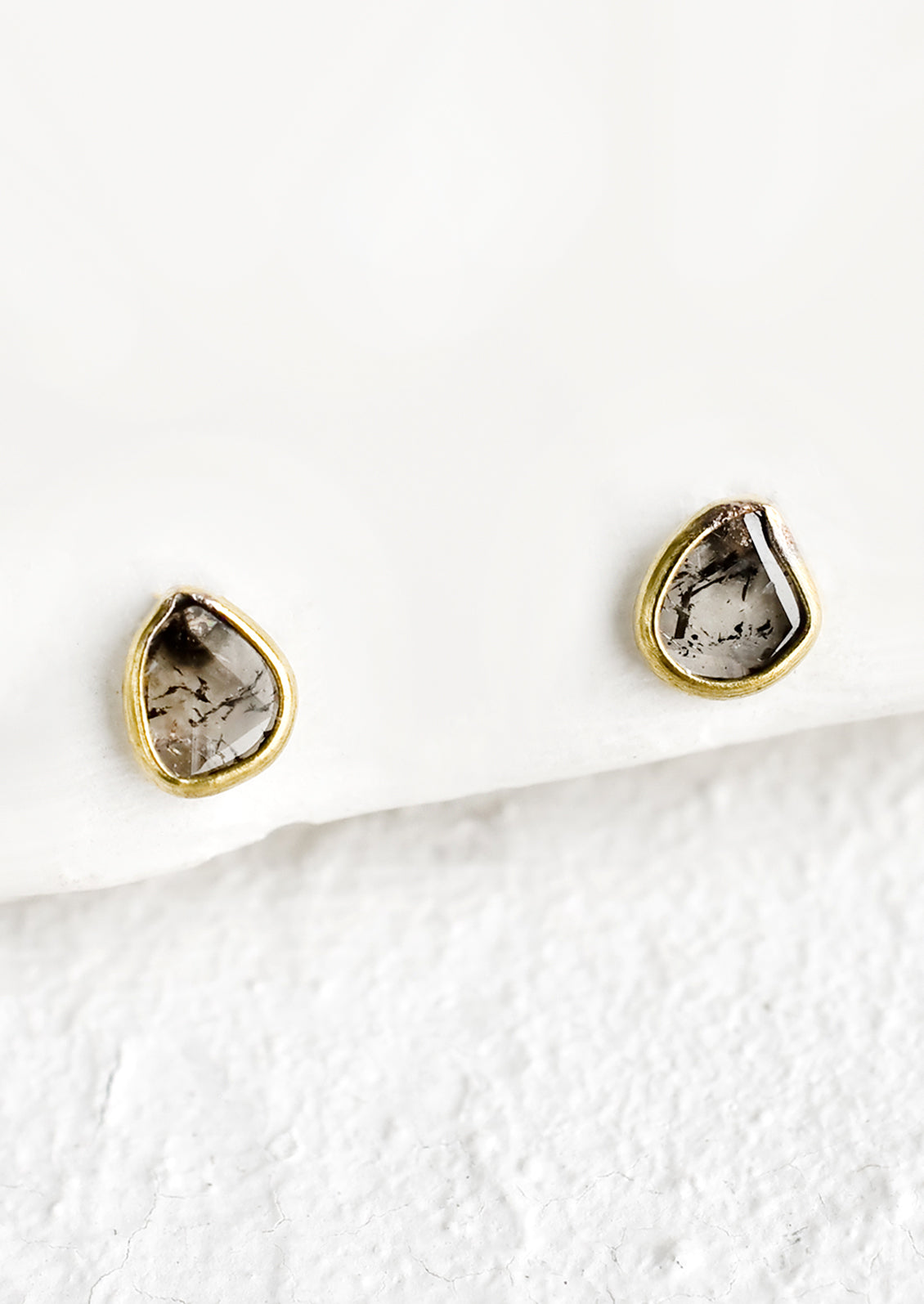 Organically shaped stud earrings with small diamond slice surrounded by brass metal trim