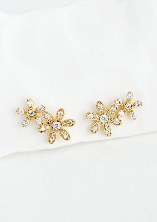 A pair of gold stud earrings in a two flower silhouette with clear crystal detailing.