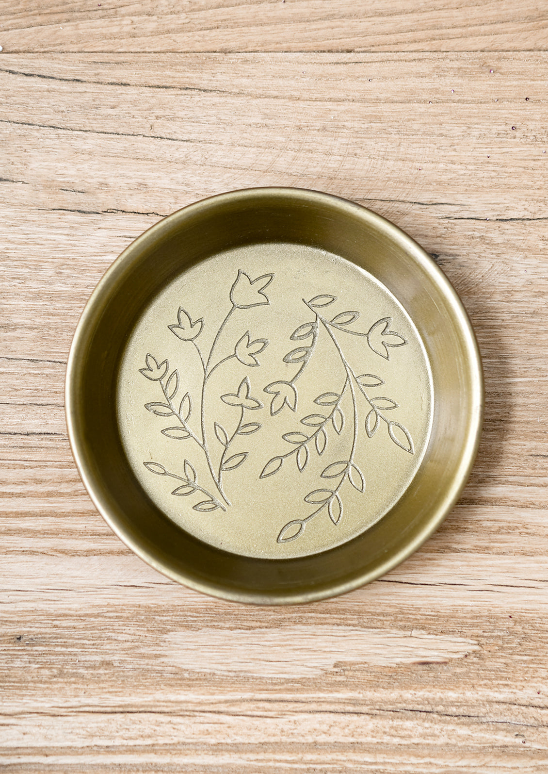 A small, round and shallow brass dish with floral engraving.