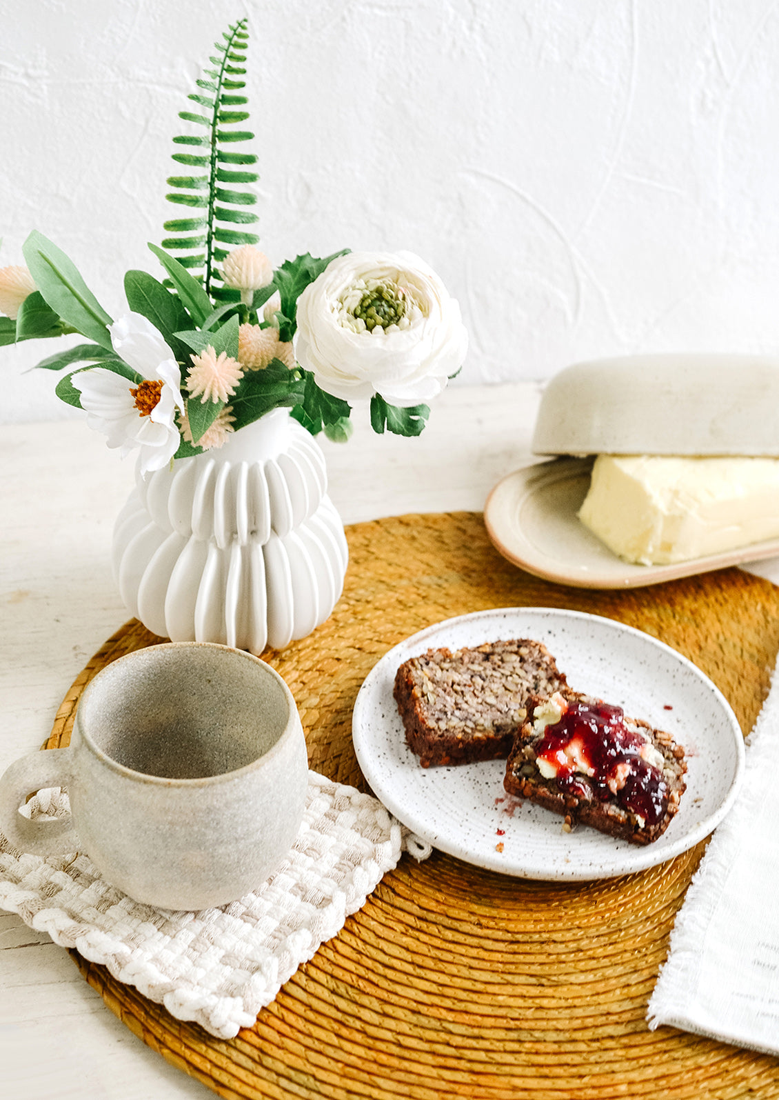 An arrangement of ceramic tableware and a vase atop a woven placemat.