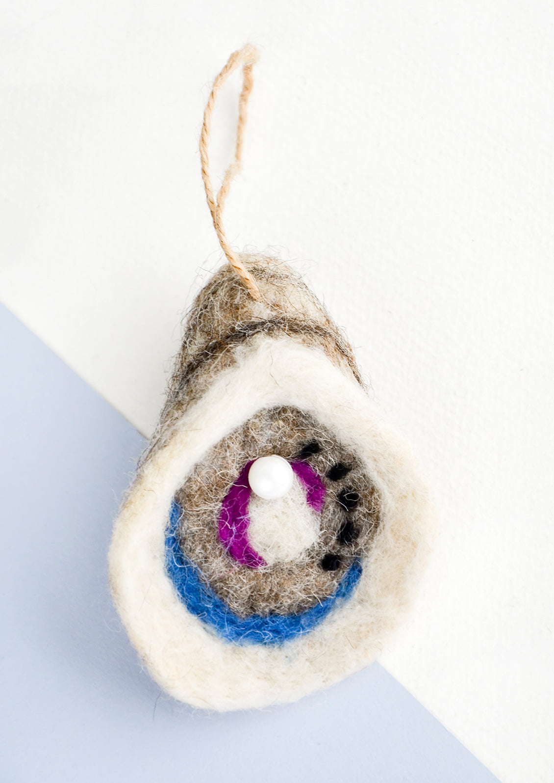 A holiday ornament in felted wool designed to look like an oyster with pearl.