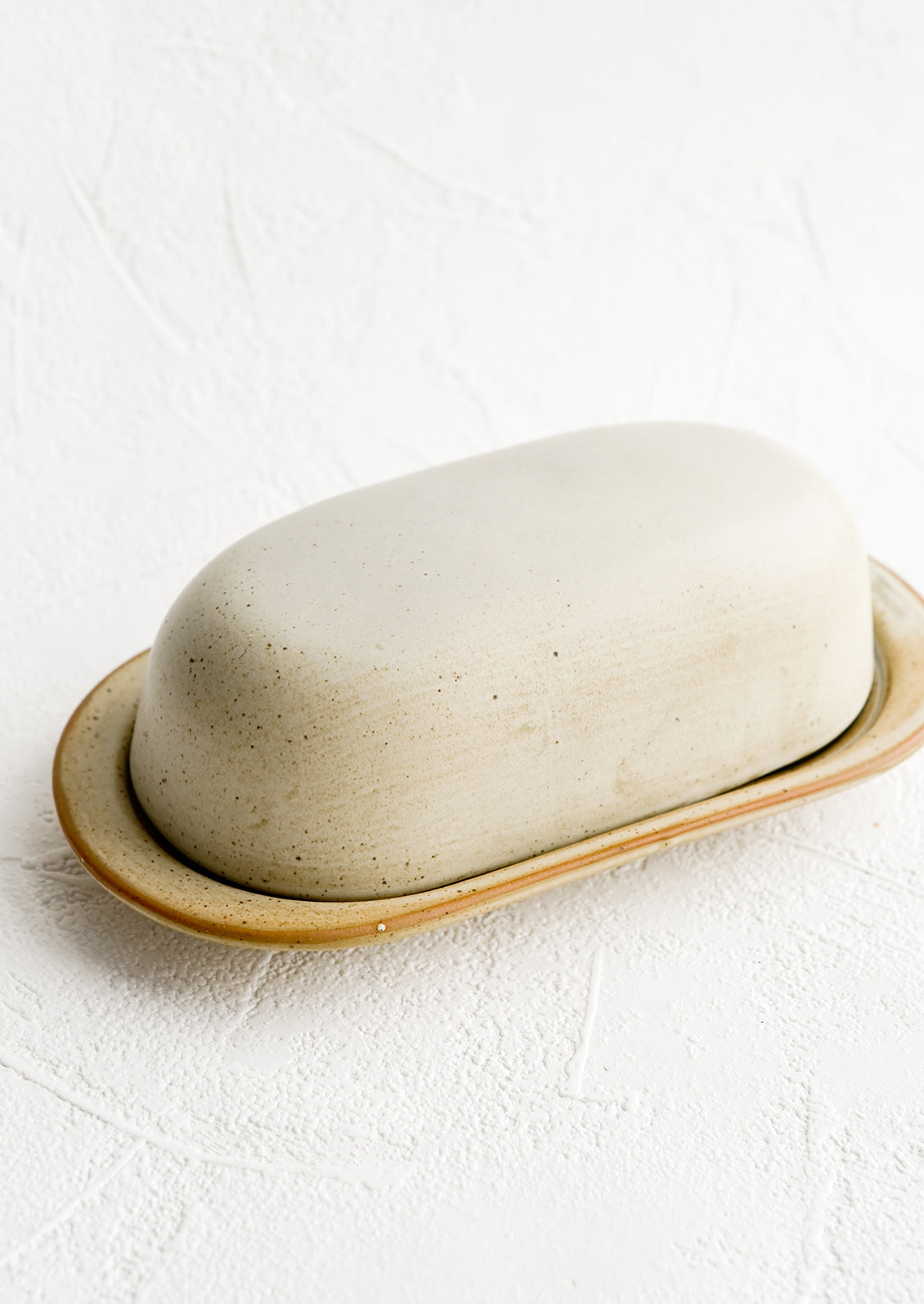 An oblong ceramic butter dish and tray in a softly speckled tan glaze.