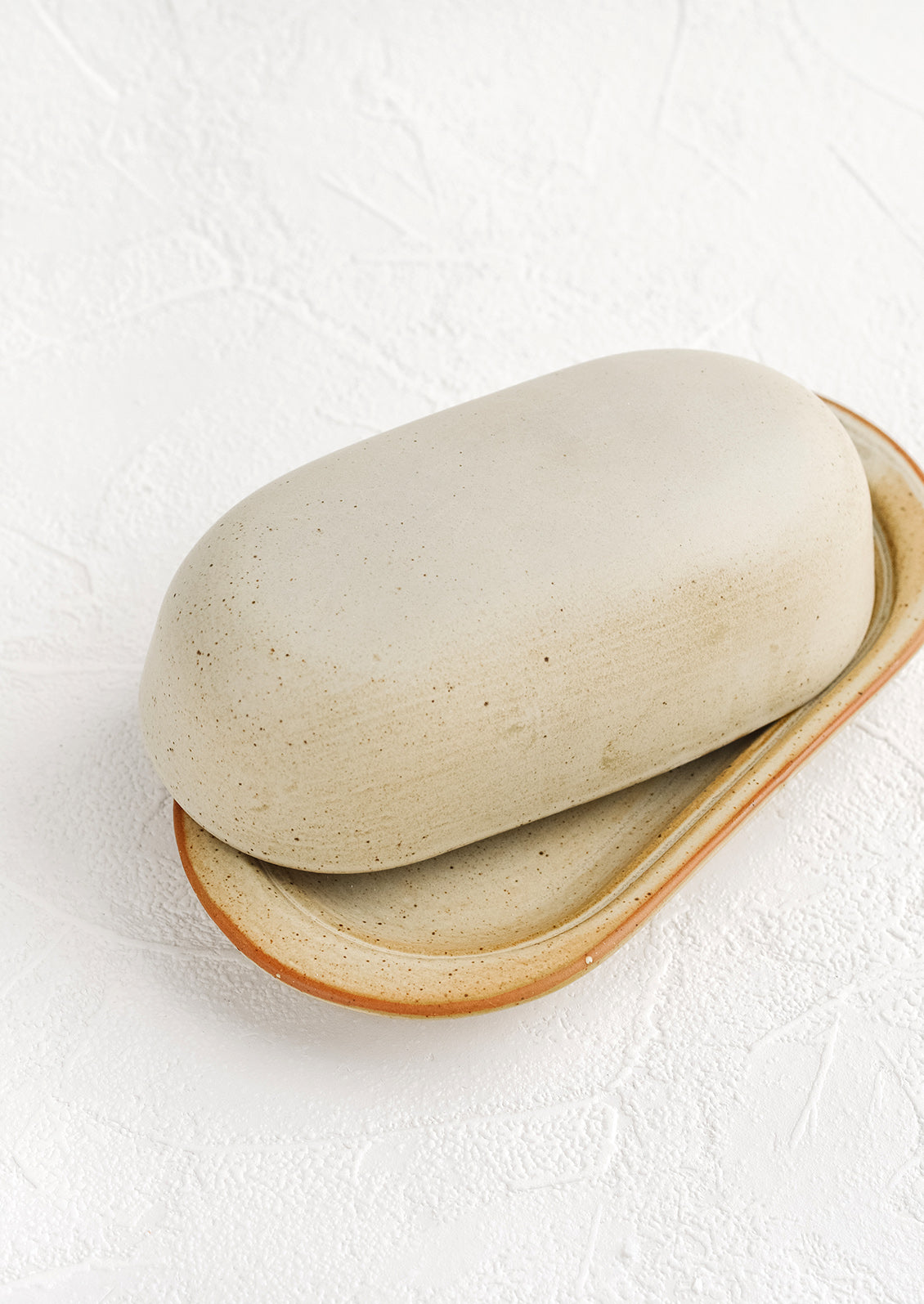 An oblong ceramic butter dish and tray in a softly speckled tan glaze.