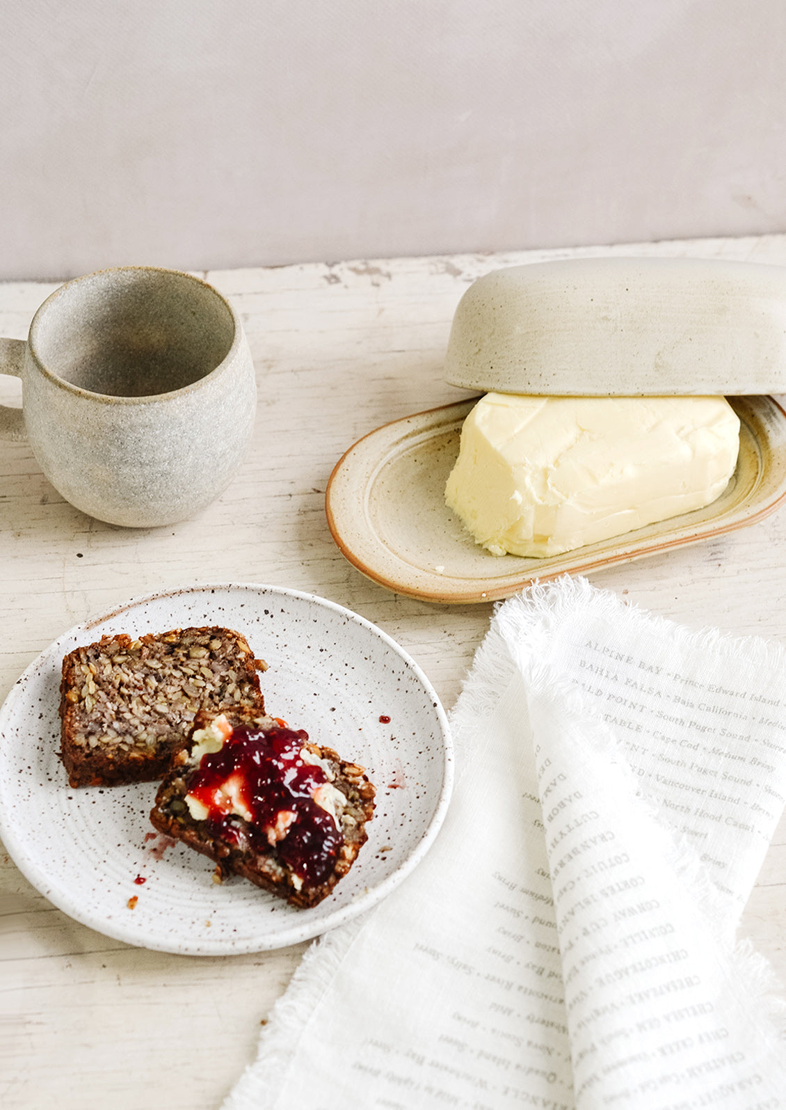 A breakfast tableware scene with coffee mug, butter dish and toast and jam on a ceramic plate.