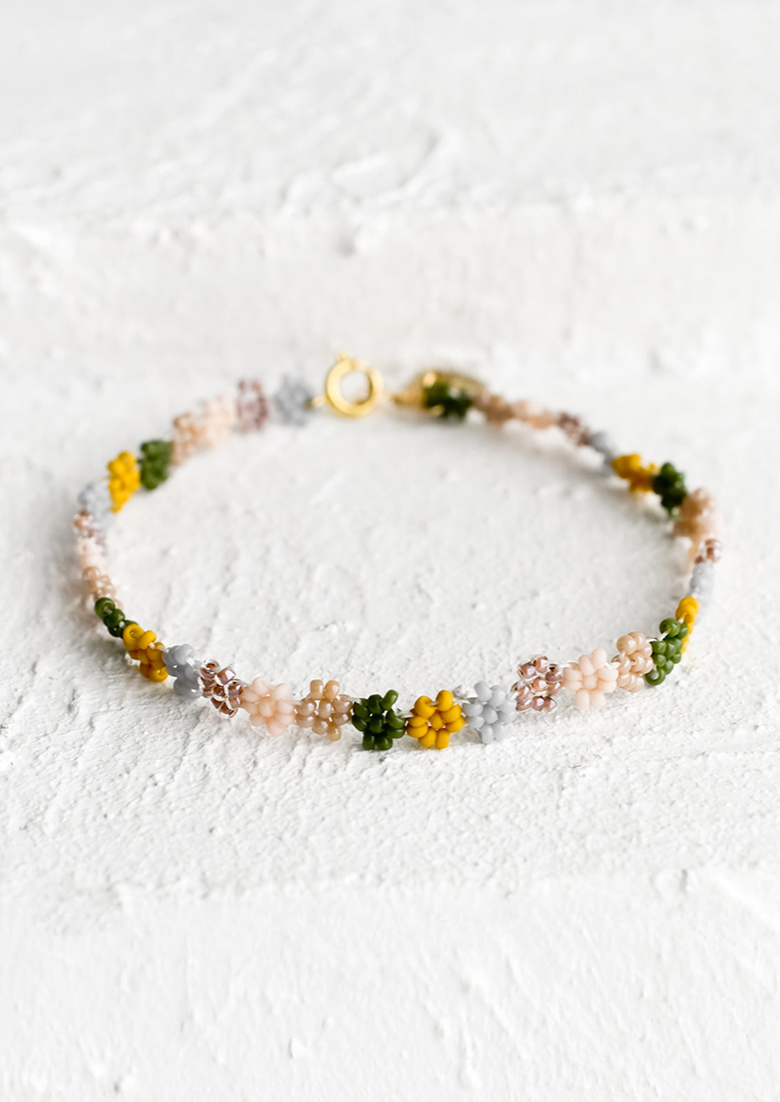 A beaded bracelet in flower shape in dusty pink, mustard, grey and olive.