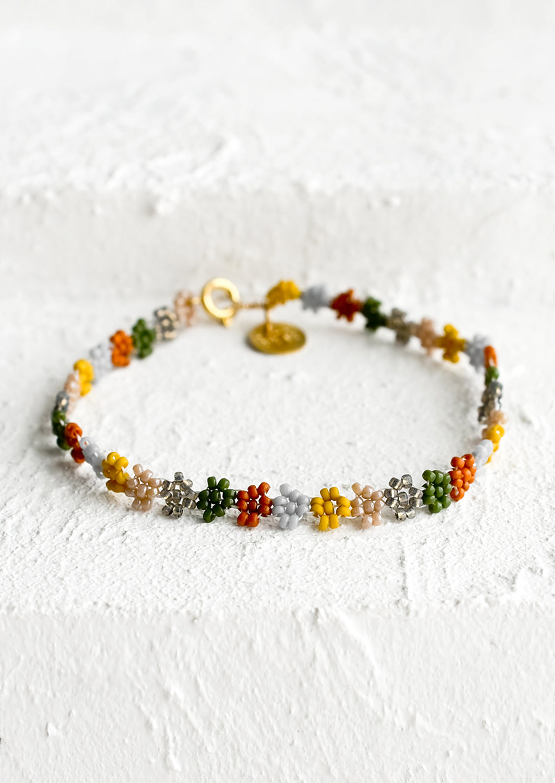 A beaded bracelet in flower shape in rust, grey, mustard and olive.