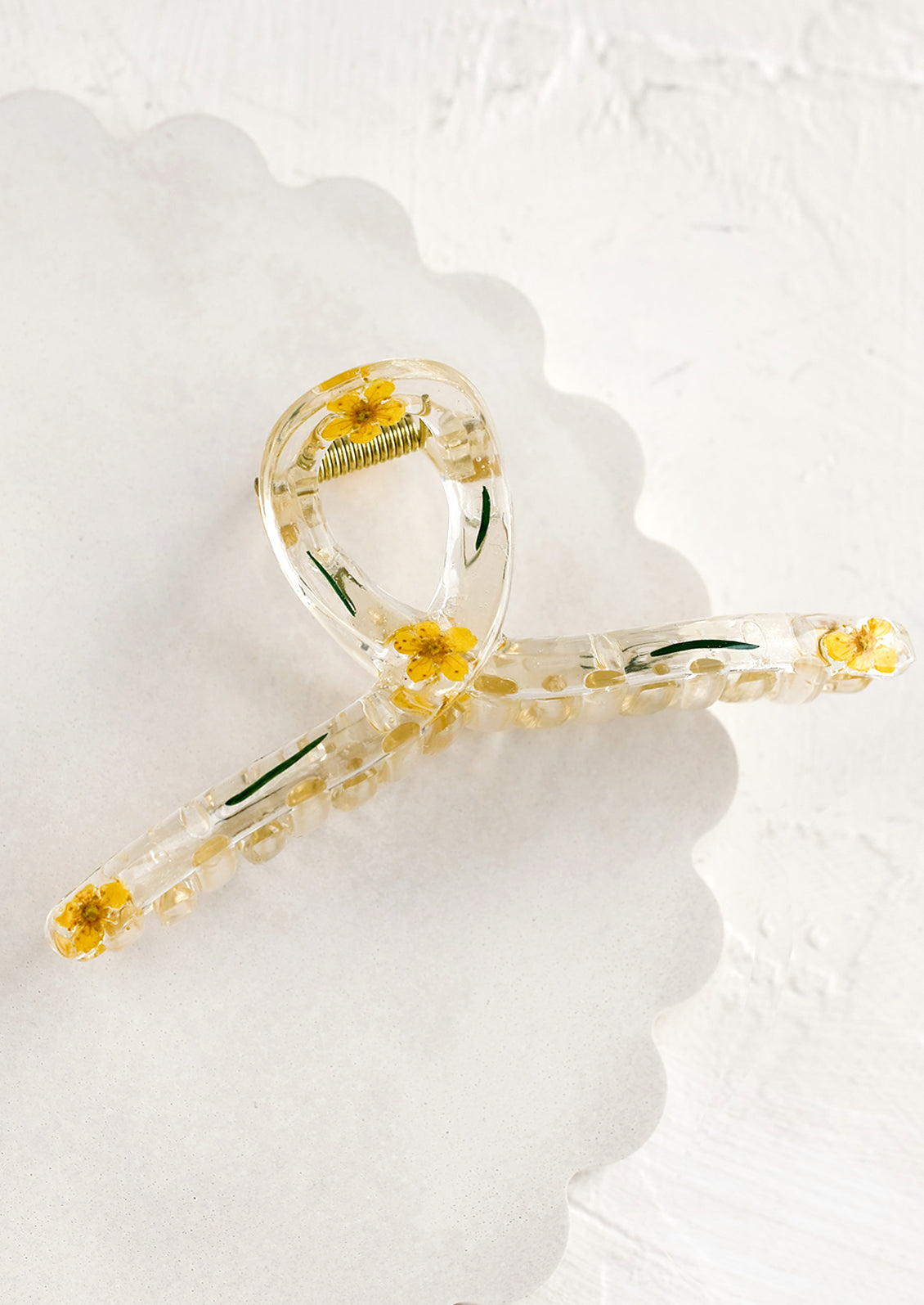 A clear crescent shaped hair claw with yellow dried flowers.