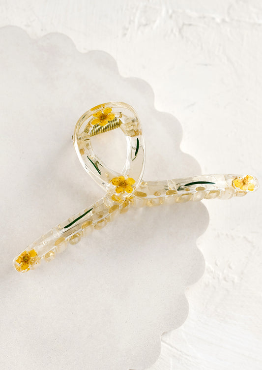 A clear crescent shaped hair claw with yellow dried flowers.