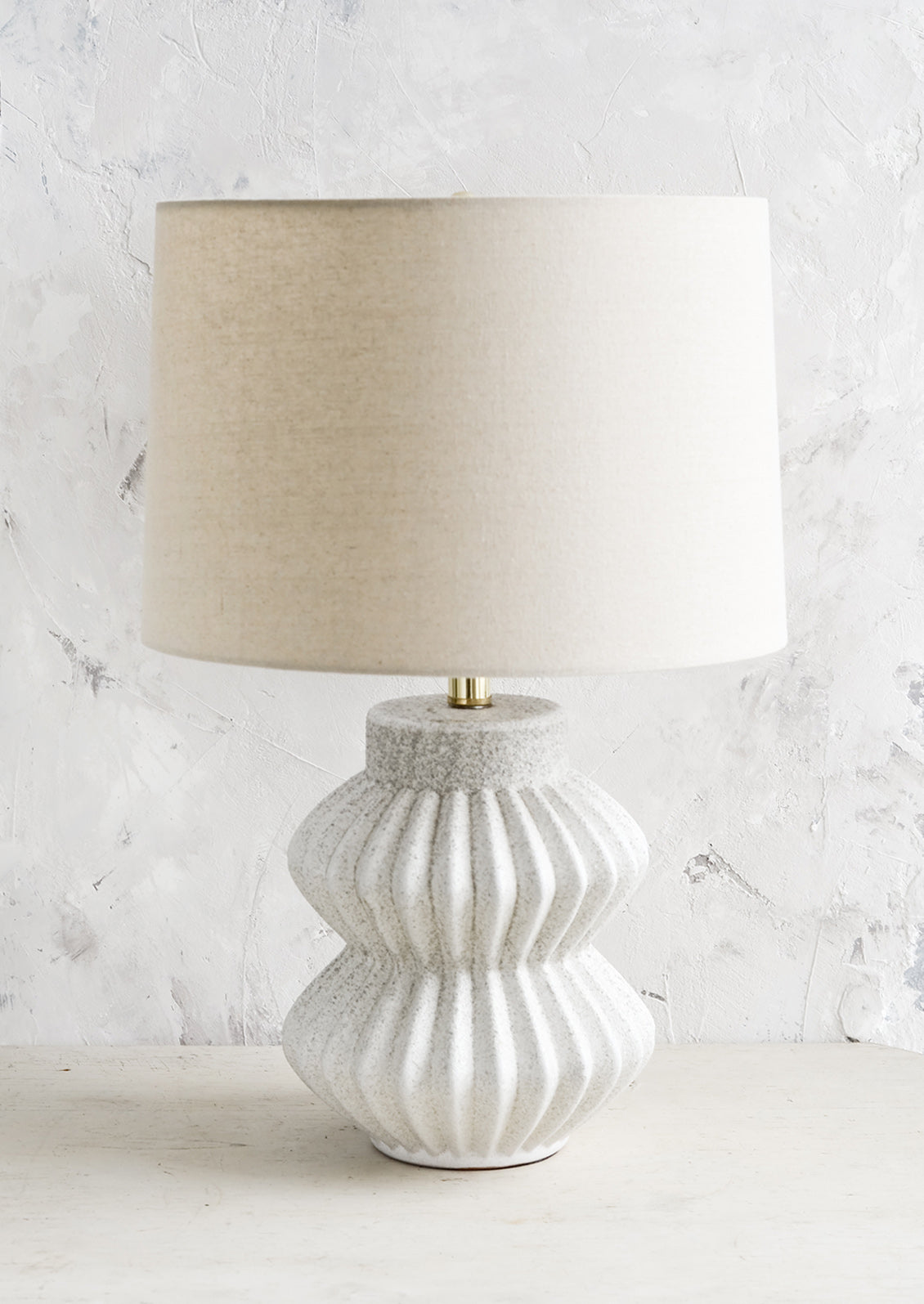 A table lamp with fluted ceramic base in speckled gray and natural linen shade.