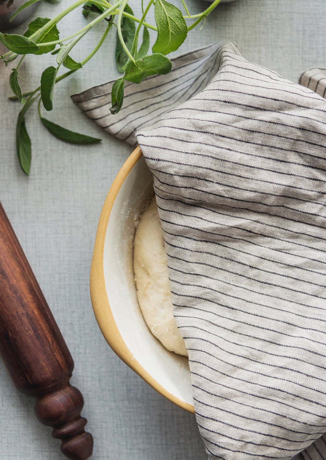 A linen tea towel in tan and black pinstripe covering a bowl of rising dough.