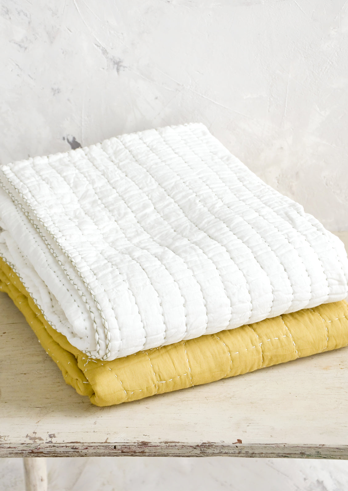 Quilted cotton throws in white and mustard, folded on a table