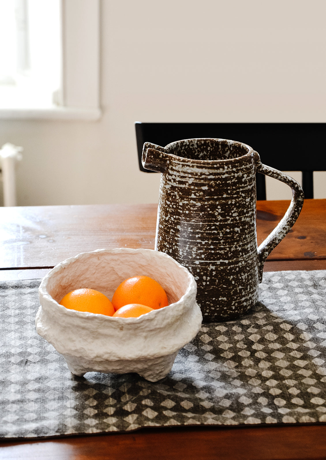 Tabletop scene with ceramic pitcher and white paper mache bowl with tangerines