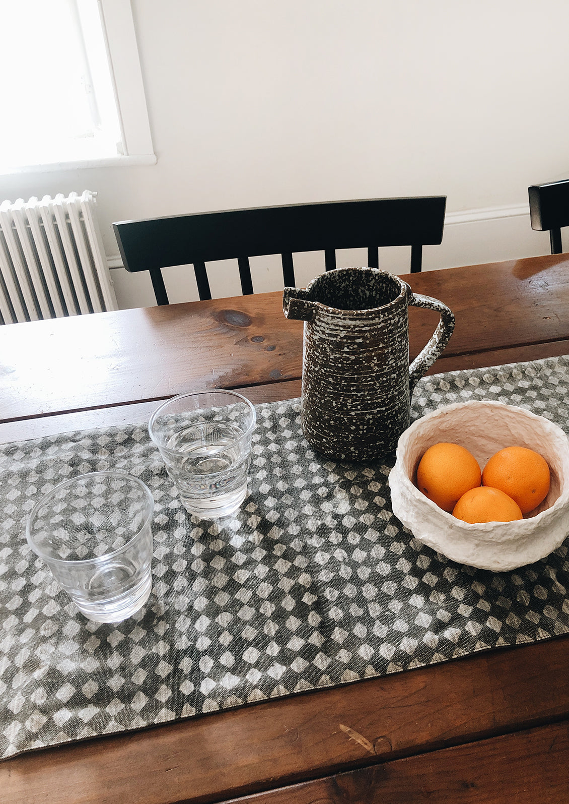 Dining table with table runner, water glasses, pitcher and bowl of oranges