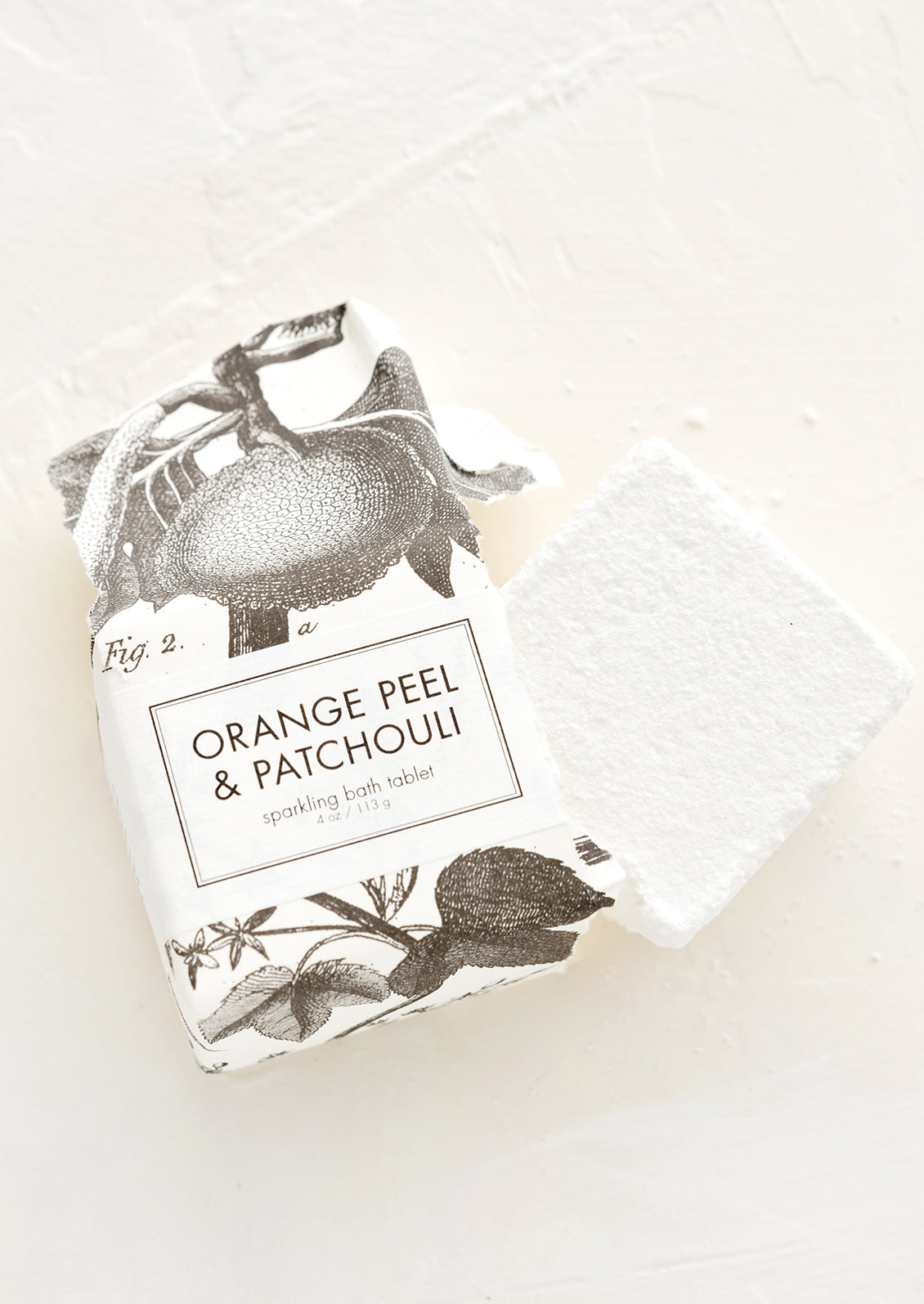 White bath fizz cube emerging from black and white botanical packaging.