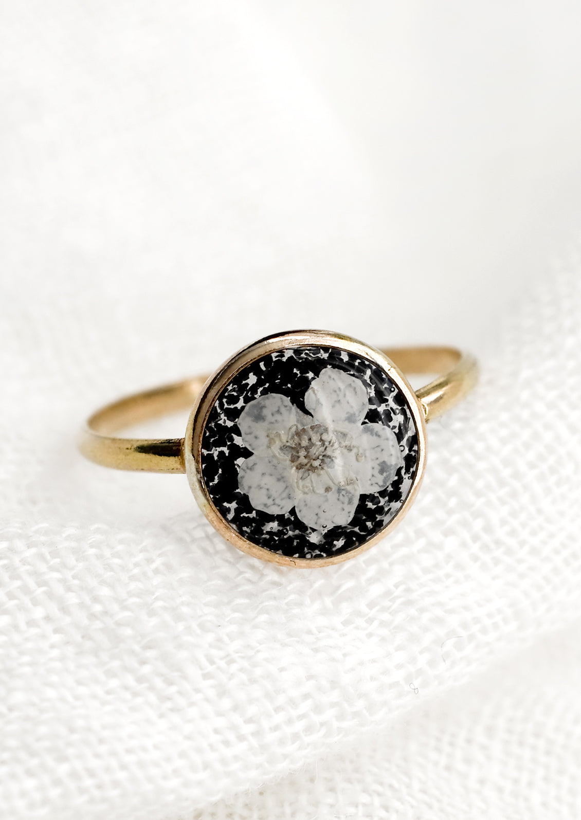 A gold round bezel ring showing white flower on black background.