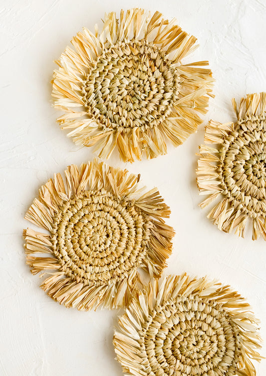 Four round straw coasters with fringed trim in natural tan.