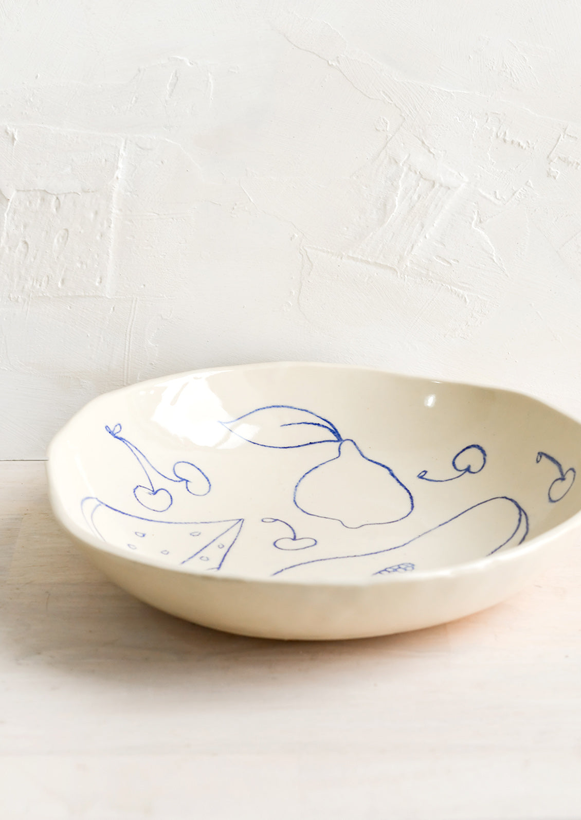 A round serving bowl in natural ceramic with blue fruit line drawings.