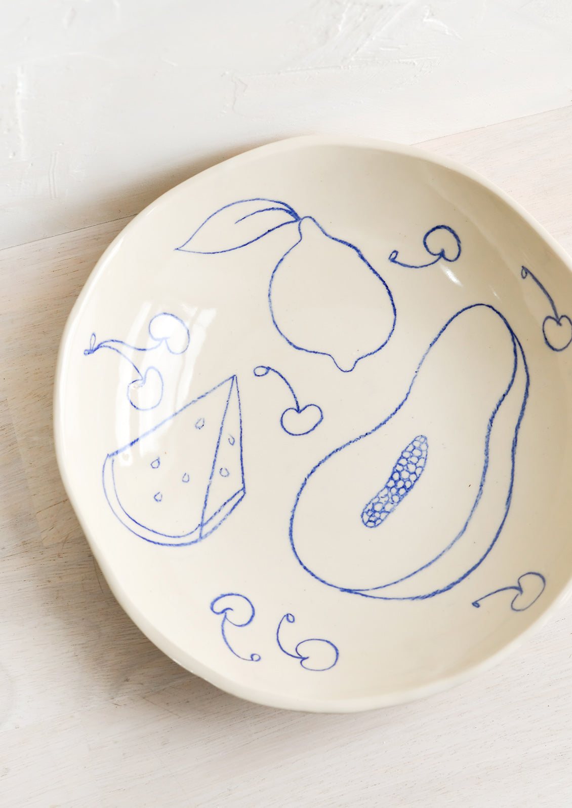 A round serving bowl in natural ceramic with blue fruit line drawings.