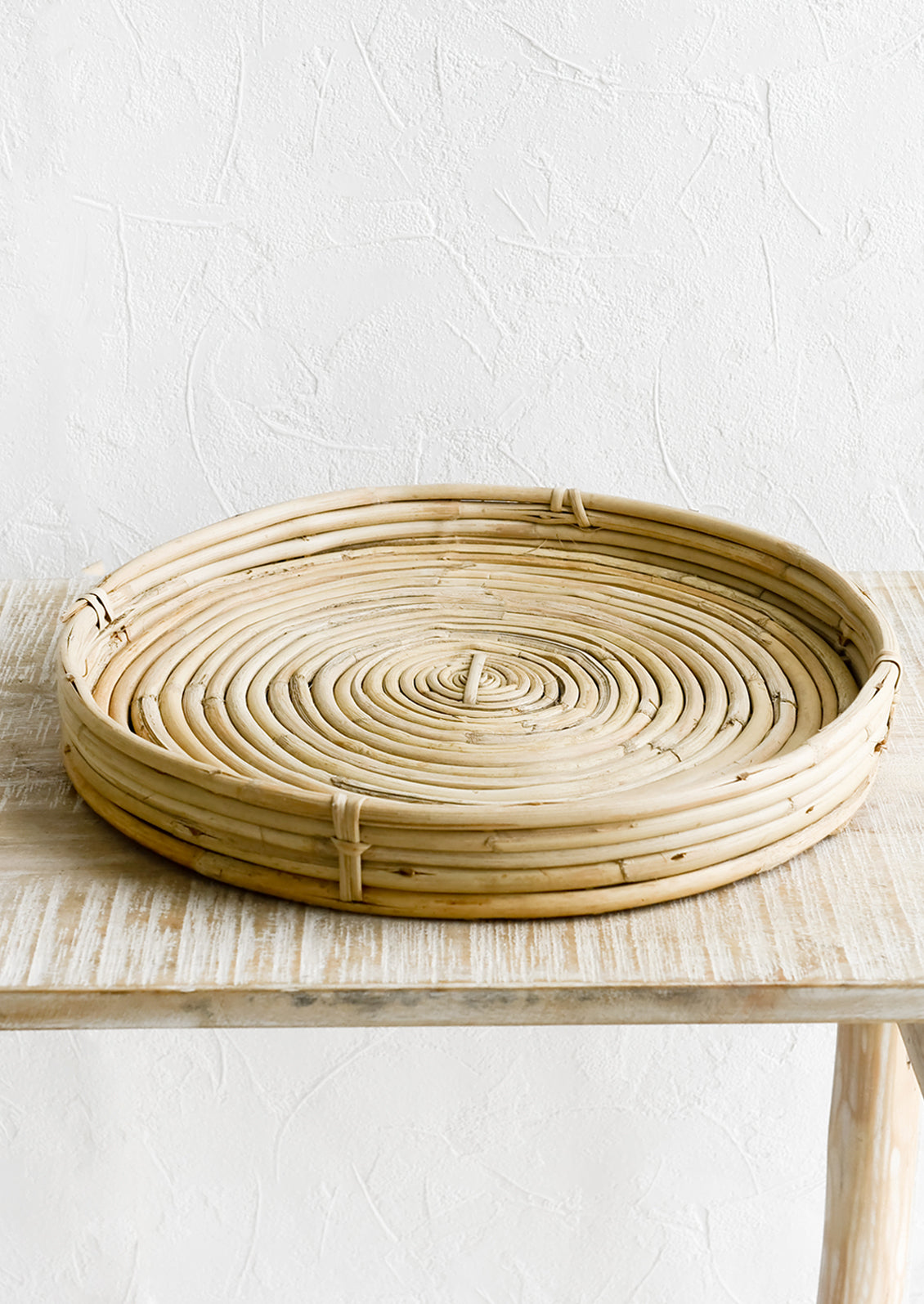 A round, shallow woven tray made from rattan.