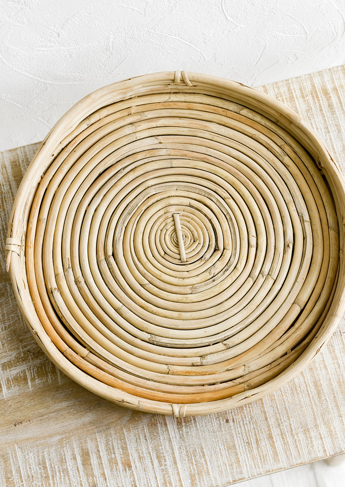 A round, shallow woven tray made from rattan.