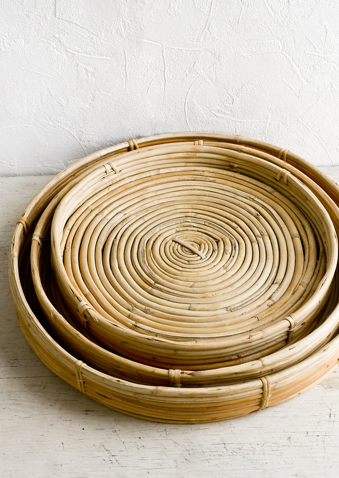 Shallow woven rattan trays in three incremental sizes.