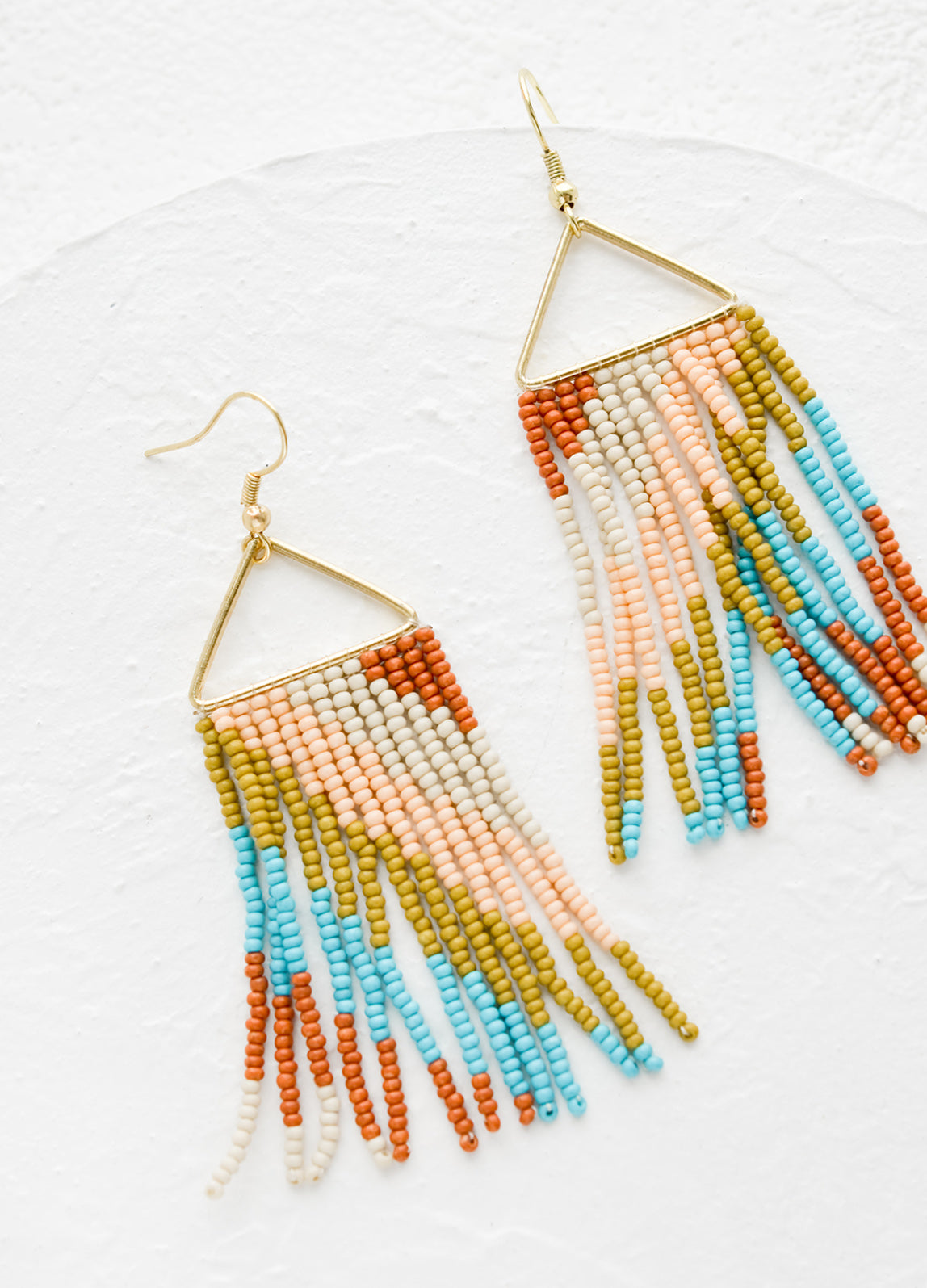 A pair of statement earrings with triangle metal top and fringe beads below.