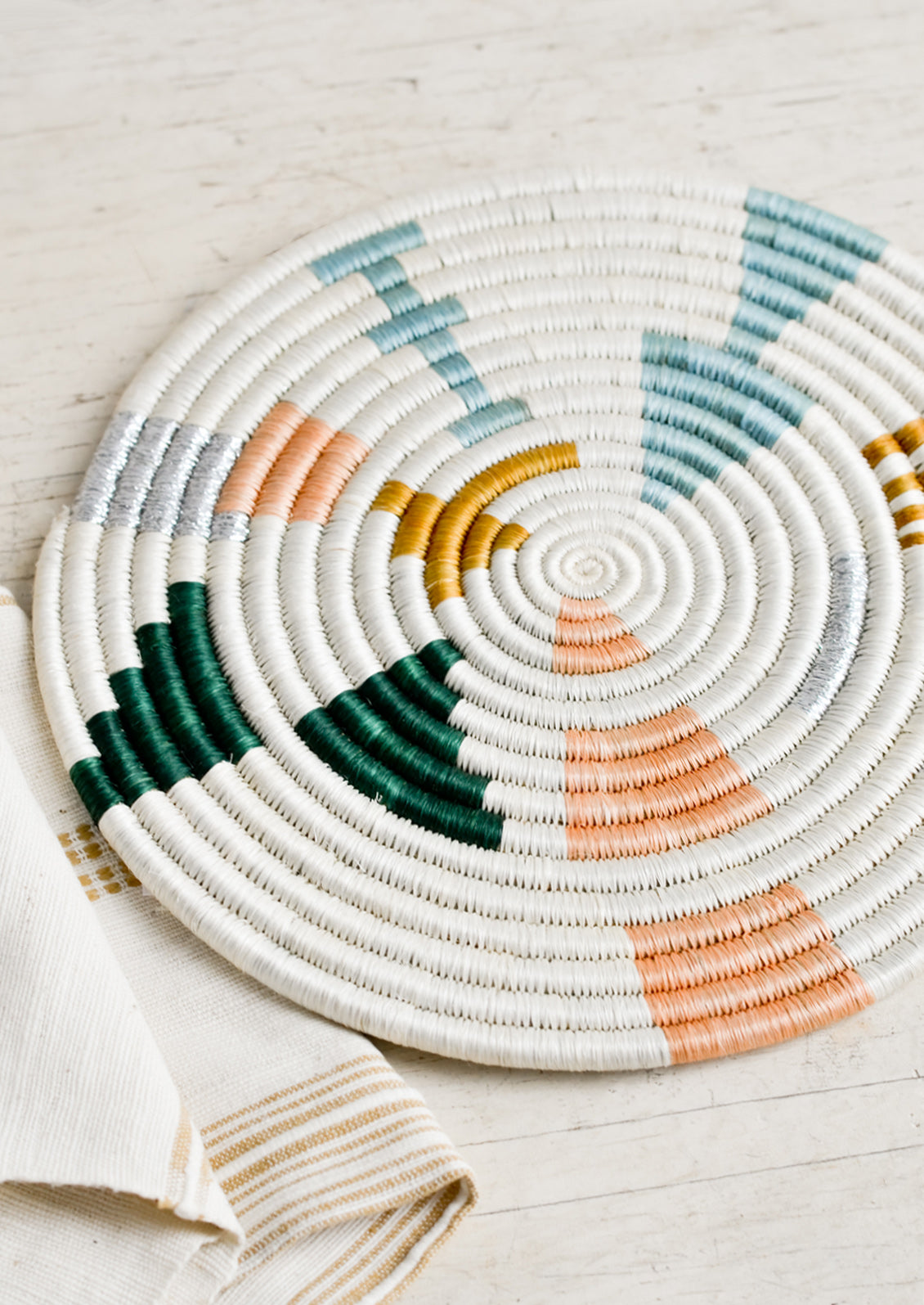 A round trivet in white with metallic and pastel design.