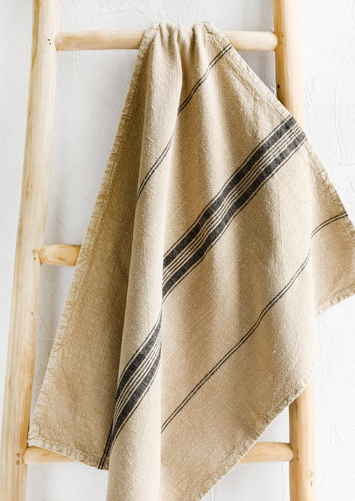 A tea towel in light tan color with stripe print down the middle.