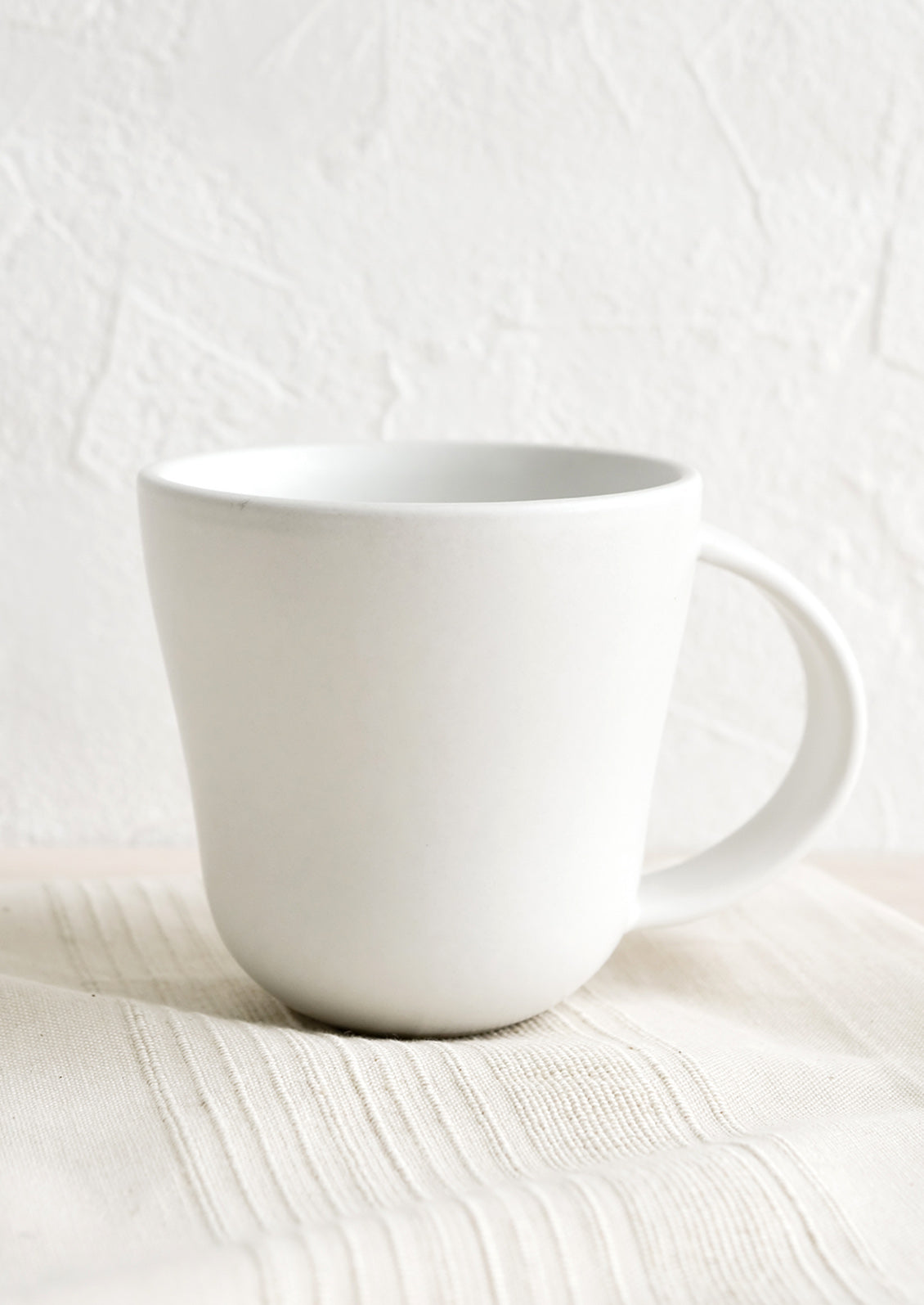 A matte white ceramic mug with softly curved shape.