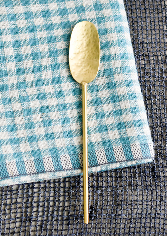 A wide and long hammered gold spoon with slim, round handle.