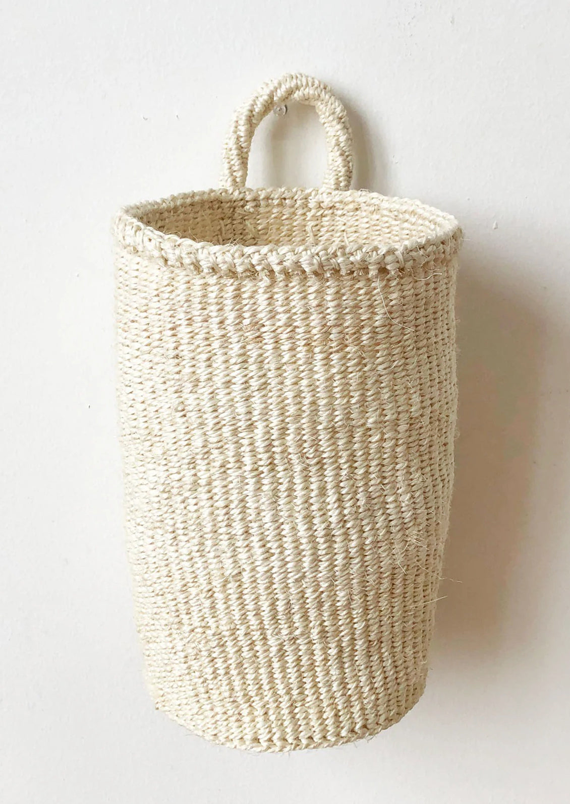 An oblong cylindrical basket woven from sisal in cream color.