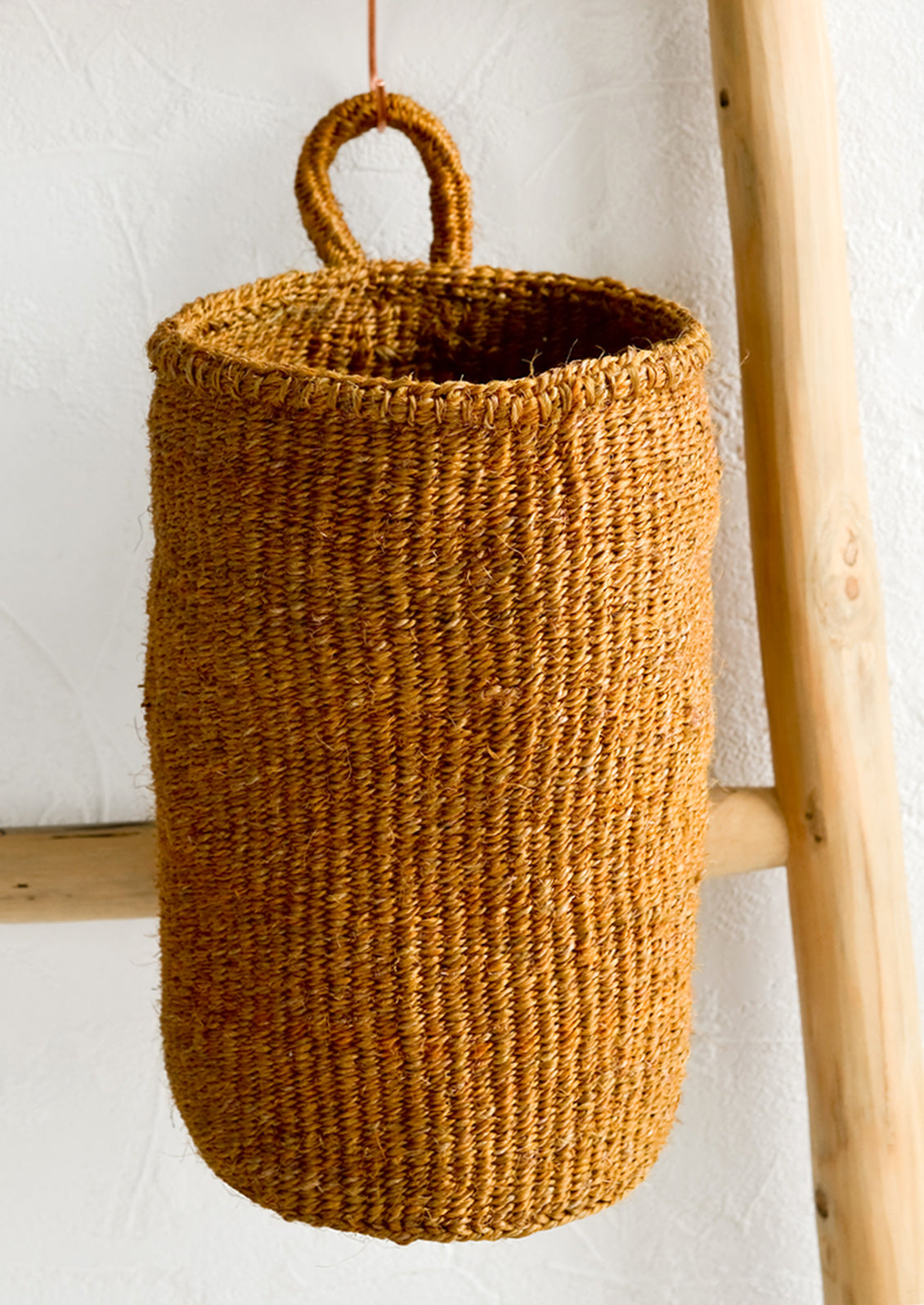 An oblong cylindrical basket woven from sisal in ochre color.