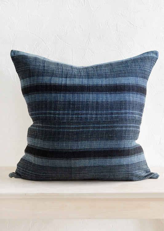 A square throw pillow in indigo fabric with variegated black stripes.