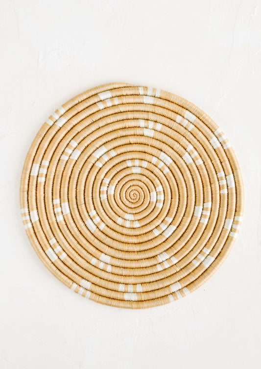 A round sweetgrass trivet in tan with white dash pattern.